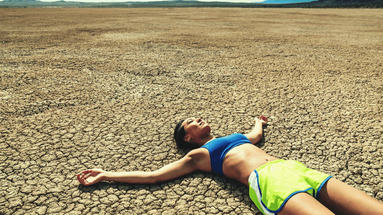 Women in workout gear laying on cracked dry desert ground with nothing around.